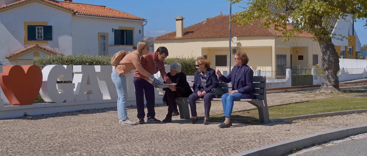 Um casal conversa com três mulheres sentadas num banco, numa praça