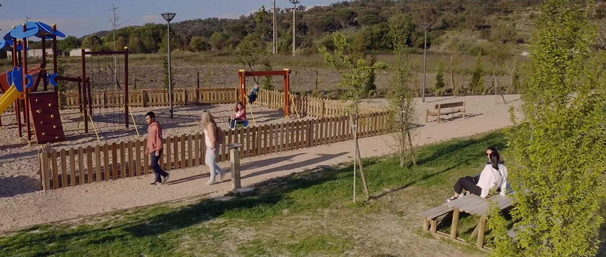 Pessoas a passear e a descansar num parque com baloiços, bancos e árvores